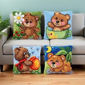 Può includere: Quattro cuscini quadrati con disegni testurizzati a punch needle di orsetti bruni. I disegni includono un orso con una margherita, un orso in una tazza verde con un anatroccolo, un orso con un vasetto di miele e un orso sotto una luna crescente.