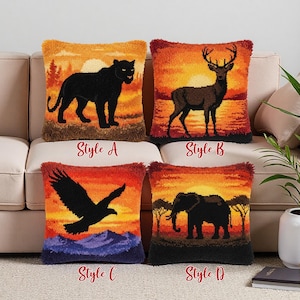 Op de afbeelding: Vier decoratieve sierkussens met dierenontwerpen. Stijlen zijn onder meer een zwarte panter, een hert met geweien, een vliegende adelaar en een olifant. Elk kussen heeft een zonsondergangachtergrond en de stijlletter.