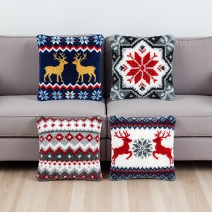 Könnte beinhalten: Vier dekorative Zierkissen mit festlichen Wintermotiven. Zwei Kissen zeigen Rentiere, Schneeflocken und geometrische Muster in Rot, Weiß, Blau und Gold. Die anderen beiden Kissen haben Schneeflocken- und geometrische Muster in Rot, Weiß und Grau.