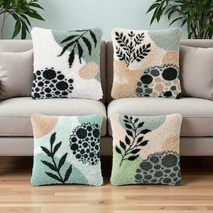 Peut inclure: Quatre coussins carrés avec des motifs botaniques abstraits. Chaque coussin présente une texture touffetée avec un mélange de couleurs, dont le blanc, le vert, le beige et le noir. Les motifs comprennent des feuilles et des pois.