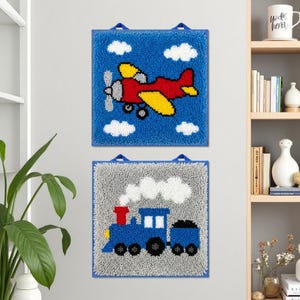 May include: Two square, textured wall hangings. The top one features a red and yellow aeroplane with white clouds on a blue background. The bottom one shows a blue train with white smoke on a grey background. Both have blue hanging loops.