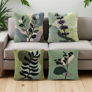 May include: Four square throw pillows with botanical designs. The pillows feature a textured, tufted appearance with various shades of green, beige, and blue. Each pillow showcases a different plant motif, including leaves and flowers, creating a nature-inspired theme.
