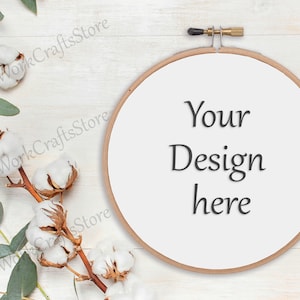 Puede incluir: Un aro de bordado blanco con el texto "Your Design here" sobre un fondo de madera blanco con una rama de bolas de algodón y hojas de eucalipto.