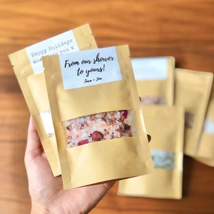 May include: A small brown paper bag filled with pink bath salts and dried rose petals. The bag has a white label that says "From our shower to yours!" with the names "Tara + Jon" printed below.