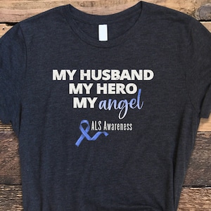 May include: Dark gray t-shirt with the text "My Husband My Hero My Angel" and a blue ribbon with the text "ALS Awareness".