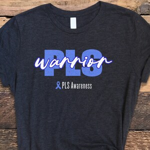 May include: A dark grey t-shirt with the text "PLS warrior" in blue lettering. The text "& PLS Awareness" is printed below the main text in a smaller font.