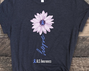 May include: A dark heather grey t-shirt with a purple daisy and a blue ribbon. The text "hope" is written vertically below the flower. The text "& ALS Awareness" is written below the word "hope".