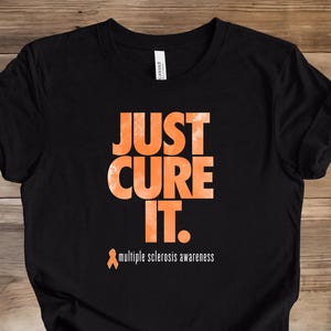 May include: Black t-shirt with orange text that reads "JUST CURE IT." and a small orange ribbon with the text "multiple sclerosis awareness".