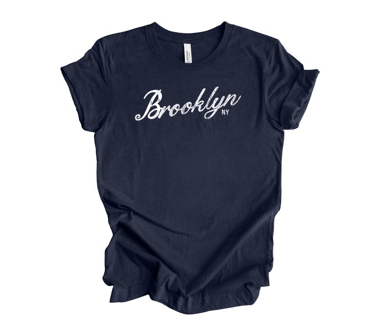 Op de afbeelding: Een marineblauw t-shirt met het woord "Brooklyn" in witte scriptletter. De afkorting "NY" staat eronder. Het t-shirt is gemaakt van zacht materiaal en heeft korte mouwen. Het t-shirt is donkerblauw.
