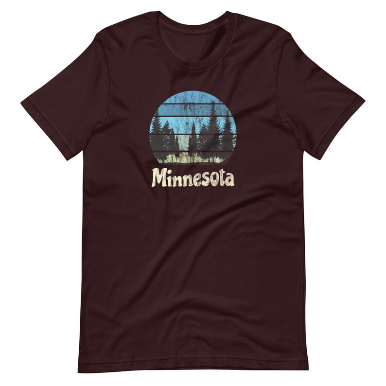 May include: A maroon t-shirt with a vintage-style graphic of a sunset behind a row of pine trees. The graphic is in shades of blue, green, and yellow. The text "Minnesota" is printed below the graphic.