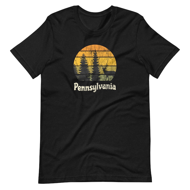Op de afbeelding: Zwart T-shirt met een vintage-zonnenonderganggrafiek met een silhouet van bomen en een hert. De tekst "Pennsylvania" is onder de grafiek gedrukt.