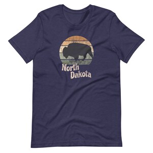 May include: A navy blue t-shirt with a vintage-style graphic of a bison silhouette in front of a sunset with the text "North Dakota".
