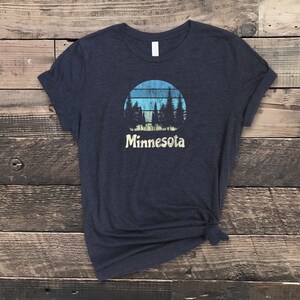 May include: A dark blue t-shirt with a vintage-style graphic of a sunset with trees and the word "Minnesota" underneath.