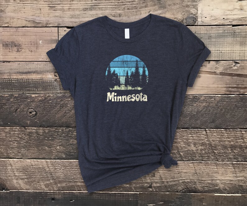 May include: A dark blue t-shirt with a vintage-style graphic of a sunset with trees and the word "Minnesota" underneath.