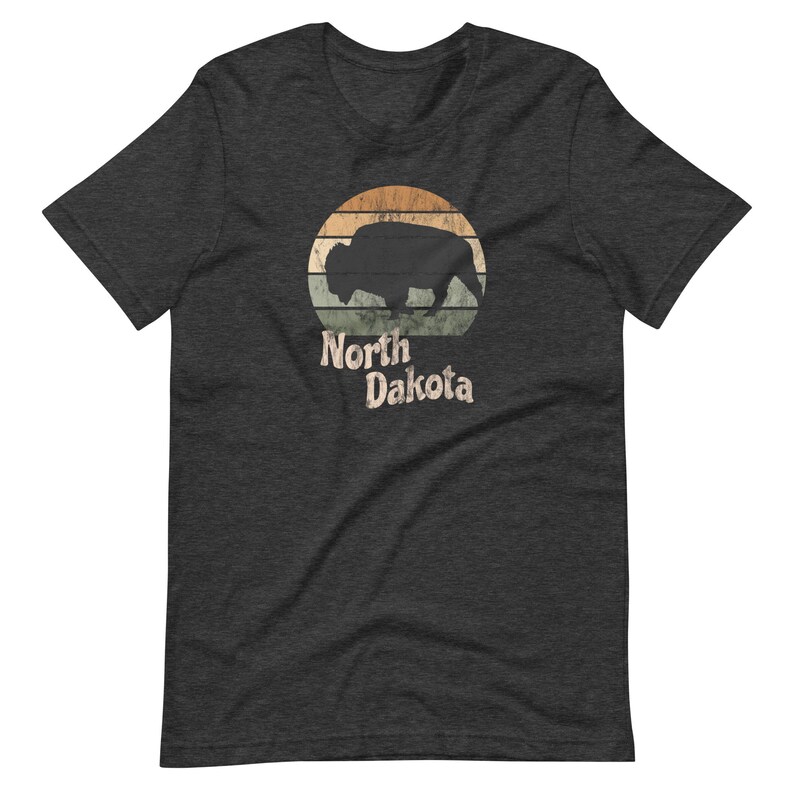 May include: A dark heather grey t-shirt with a vintage-style graphic of a bison silhouette in front of a sunset with the text "North Dakota".