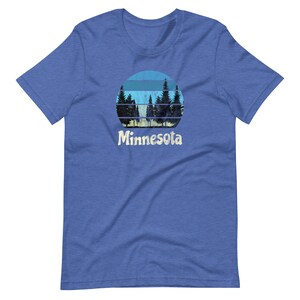 May include: A blue t-shirt with a retro-style graphic of a sunset behind a forest silhouette. The text "Minnesota" is printed below the graphic.