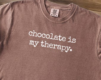 May include: A brown t-shirt with the text "chocolate is my therapy." printed in white.