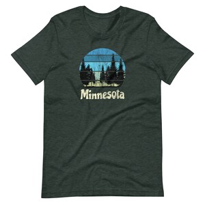 May include: A dark green t-shirt with a retro-style graphic of a blue and yellow sunset with trees in front of it. The text "Minnesota" is printed below the graphic.