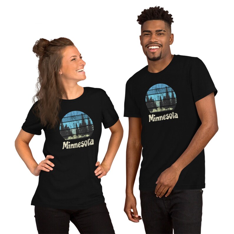 May include: Two people wearing black t-shirts with a retro-style graphic of a forest scene and the word "Minnesota".