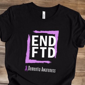 May include: Black t-shirt with a purple square frame containing the words "END FTD" in white. Below the frame is a purple ribbon and the text "Dementia Awareness".