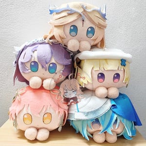 May include: A stack of five plush dolls with large eyes and various hair colors, including blonde, purple, and pink. Each doll has a unique outfit and design, with a small charm featuring a cartoon character.