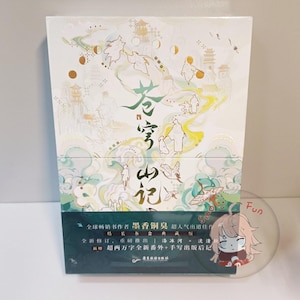 Puede incluir: Un juego de libros en caja con un diseño blanco, verde y dorado. La parte superior presenta ilustraciones de figuras y edificios. La sección inferior tiene texto en chino. Una pegatina transparente con un personaje de dibujos animados está en primer plano.