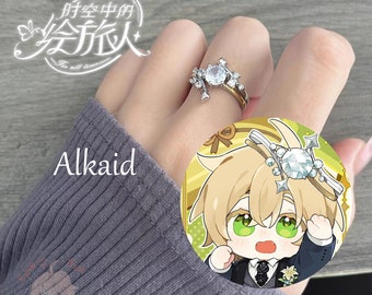 May include: A silver ring with a large clear crystal and smaller crystals set in a starburst design. The ring is on a hand wearing a grey sweater. The text "Alkaid" is visible below the ring.