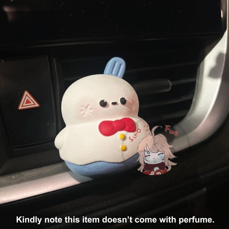 May include: A white, round, plush toy with a red bow tie and blue pants. The toy has a small, blue, pointed hat on its head. The toy is sitting in a car's air vent. The text "Sino" is visible on the toy's chest. The text "Fun" is visible in the background.