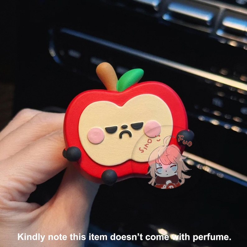 May include: A red apple-shaped car air freshener with a cute cartoon face. The apple has a frown and black eyes. The air freshener is made of soft, squishy material.