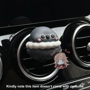 Puede incluir: Un ambientador de coche negro y blanco con forma de pingüino con un cuello blanco y esponjoso. El ambientador está sujeto a la ventilación de un coche. El texto "Fun" y "Smo" es visible en el ambientador.