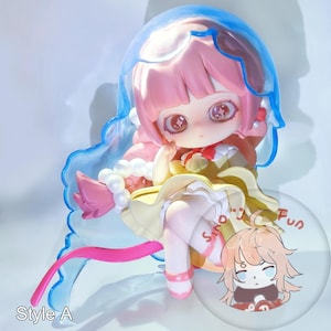 May include: A detailed figurine of a cartoon character with pink hair and large eyes. The figure is wearing a yellow dress and has a blue translucent headpiece. The base has the words "Sino Fun" and "Style A".