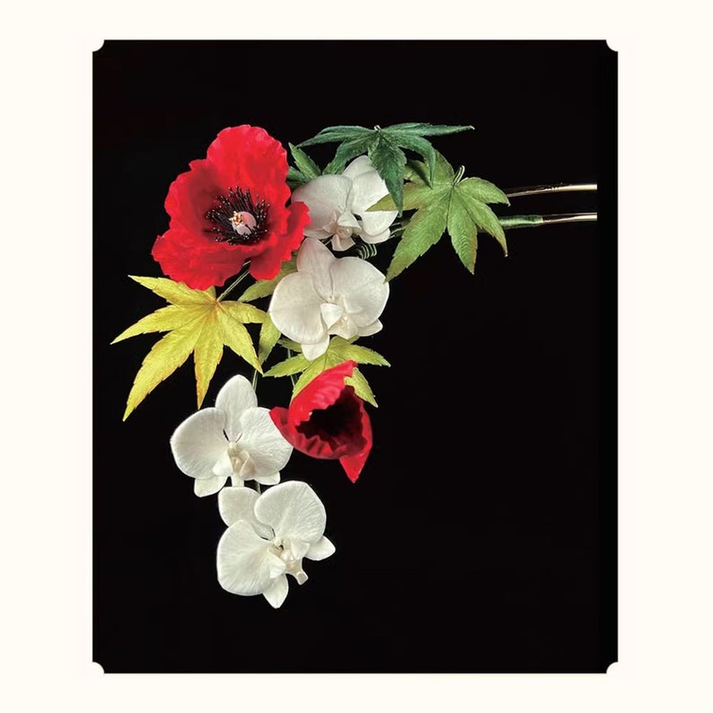 May include: A floral hair accessory featuring red poppies, white orchids, and green and yellow maple leaves. The flowers are arranged on a gold-toned hairpin against a black background. This decorative hairpiece is suitable for special occasions.