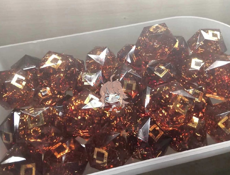 May include: A close-up of a container filled with many brown and gold dice. The dice are made of clear glass with gold flecks and have a geometric design.
