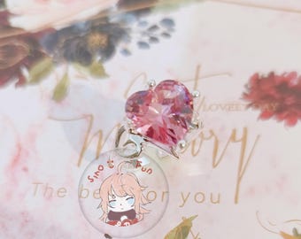 May include: A silver ring with a large, heart-shaped pink gemstone. Below the heart is a clear, round charm with a cartoon illustration and the text "Sino Fun". The background features floral designs and the words "Lovely Day".