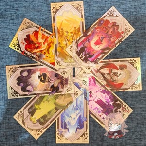 May include: A selection of tarot cards with vibrant illustrations and decorative borders. Each card displays distinct artwork, featuring figures, landscapes, and symbolic imagery. The cards are arranged in a circular pattern on a blue surface.