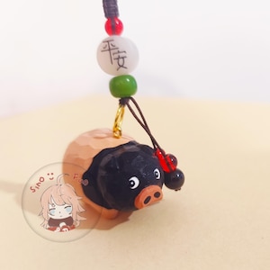 May include: A wooden pig figurine with a black body and tan head, attached to a cord with beads. The pig has a small pink snout and white eyes. A white bead with Chinese characters is above the pig.
