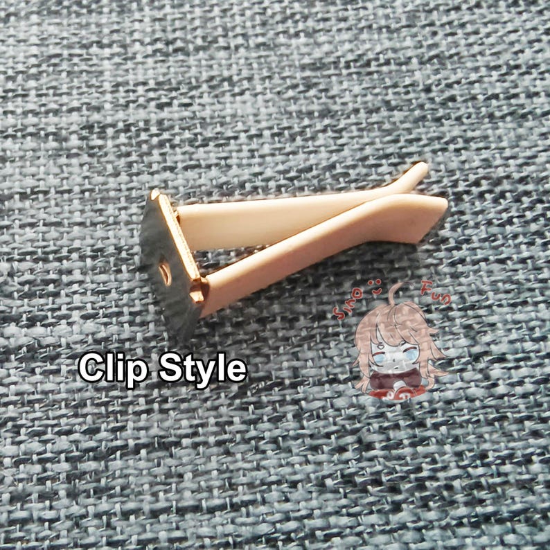 May include: A white plastic clip with a metal base. The clip is designed to hold papers or other items together. The clip is on a gray textured surface.