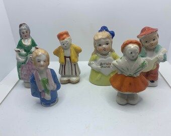 Puede incluir: Conjunto de seis figuritas de porcelana vintage que representan a varios personajes. Las figuritas están pintadas en colores brillantes, incluyendo rojo, amarillo, azul, verde y naranja. Una figurita sostiene un corazón con el texto "Je t'aime France".