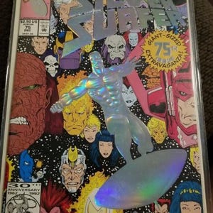 May include: A Silver Surfer comic book cover with a holographic image of the character surfing. The cover features various comic book characters and the text "The Herald Ordeal" and "Giant-Sized 75th Extravaganza!"
