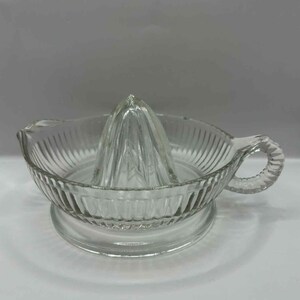 Peut inclure: Presse-agrumes en verre transparent avec un bol rainuré, un presse-agrumes conique et une poignée. Le presse-agrumes repose sur une base ronde. Design simple et fonctionnel, pour la cuisine.