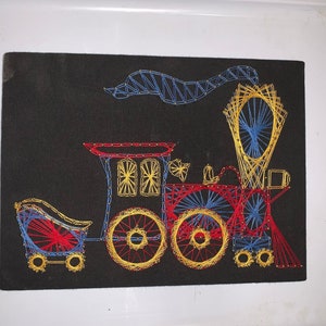 May include: A colorful string art piece depicting a train engine with a red, yellow, and blue color scheme. The train has a large smoke stack and four wheels.