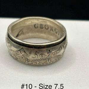 May include: A silver ring with the word "GEORGIA" engraved on the inside. The ring is decorated with intricate designs and the text "50 CENTS". The ring size is 7.5.