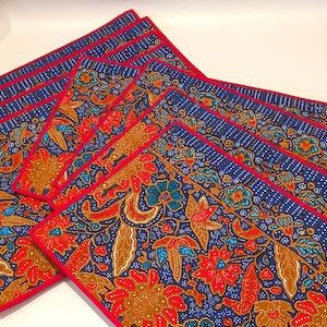 Könnte beinhalten: Eine Reihe rechteckiger Tischsets mit floralem Muster. Jedes Tischset zeigt ein Batik-Muster in Rot, Blau und Gold mit einem roten Rand. Geeignet für die Dekoration des Esstisches.
