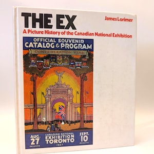 May include: A hardcover book titled "THE EX" with the text "A Picture History of the Canadian National Exhibition." The cover features a colorful illustration of a building with a Canadian flag and the text "OFFICIAL SOUVENIR CATALOG & PROGRAM."