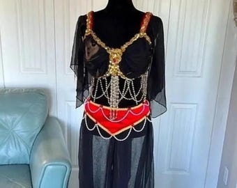 May include: Black belly dance costume with gold and red accents. The top features gold embellishments and a red belt. The costume includes a black skirt and sheer sleeves. The outfit is displayed on a black mannequin.
