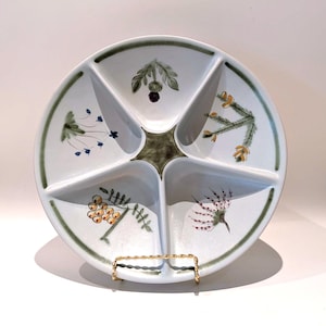 May include: A white ceramic divided serving dish with five distinct sections. The centre features a dark green star shape, and each section is decorated with a different botanical illustration of wildflowers and berries in green, yellow, and blue.