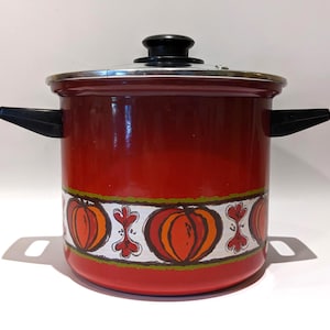 Może przedstawiać: Czerwony emaliowany garnek z pokrywką i czarnymi uchwytami. Garnek posiada ozdobny pas z pomarańczowymi dyniami i białymi akcentami. Garnek jest przeznaczony do gotowania i ma błyszczące wykończenie.