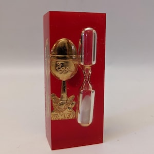 Könnte beinhalten: Ein roter Acryl-Eieruhr mit einem goldenen Ei und einer kleinen Sanduhr. Das Ei trägt die Aufschrift "Egg" und die Basis des Timers lautet "Timer".