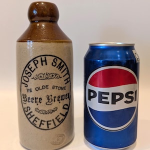 May include: An antique brown and tan stoneware bottle with the text "JOSEPH SMITH YE OLDE STONE Beer Brewer SHEFFIELD" next to a blue Pepsi can with a red and white logo.