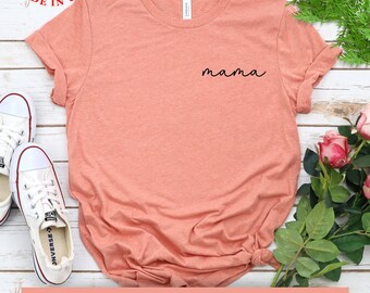 以下が含まれることがあります： 前面に黒い筆記体で「mama」と書かれたピーチ色のTシャツ。米国製で、10色、S～2XLサイズ展開。満足保証付きです。